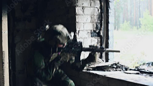 Military soldier in the form holds in the hands an assault rifle, check possible enemies around the corner