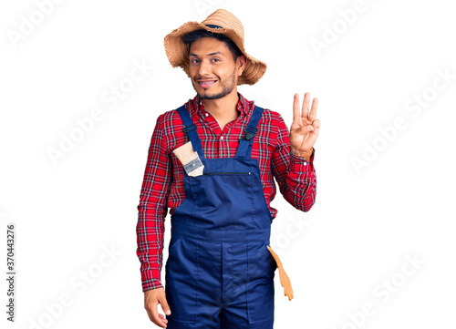 Handsome latin american young man weaing handyman uniform showing and pointing up with fingers number three while smiling confident and happy.