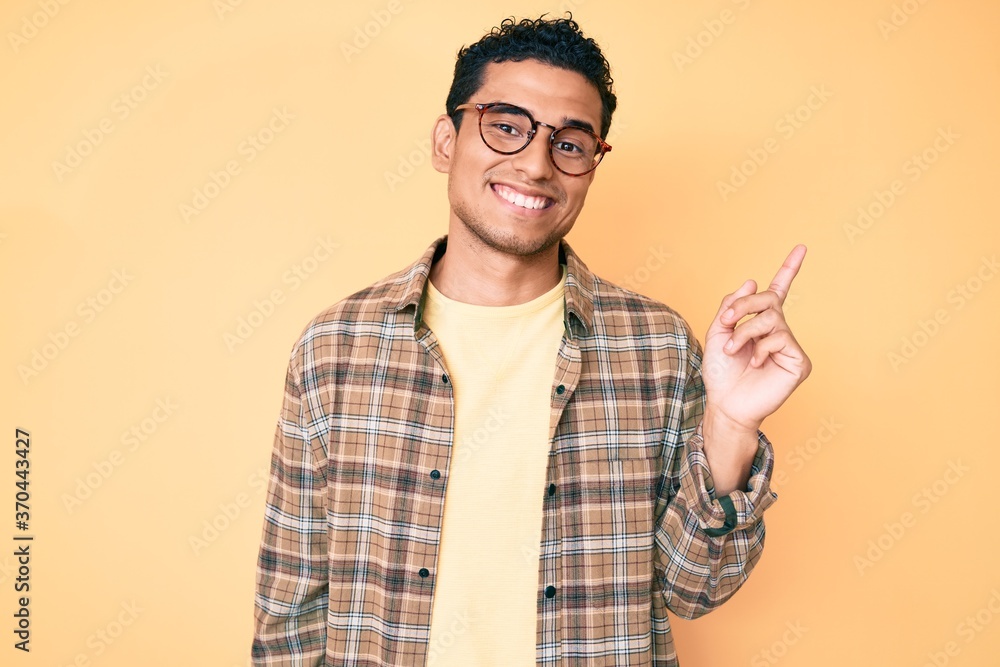 Young handsome hispanic man wearing casual clothes and glasses smiling happy pointing with hand and finger to the side Young handsome hispanic man wearing casual clothes and glasses smiling happy pointing with hand and finger to the side