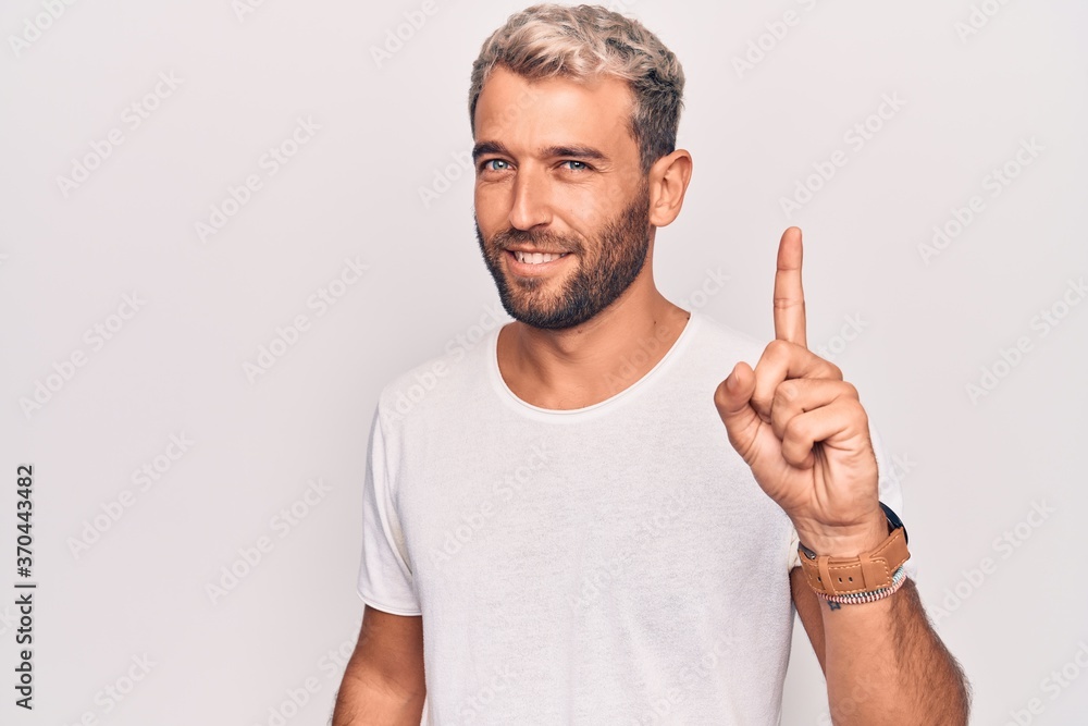Young handsome blond man wearing casual t-shirt standing over isolated white background smiling with an idea or question pointing finger up with happy face, number one Young handsome blond man wearing casual t-shirt standing over isolated white background smiling with an idea or question pointing finger up with happy face, number one