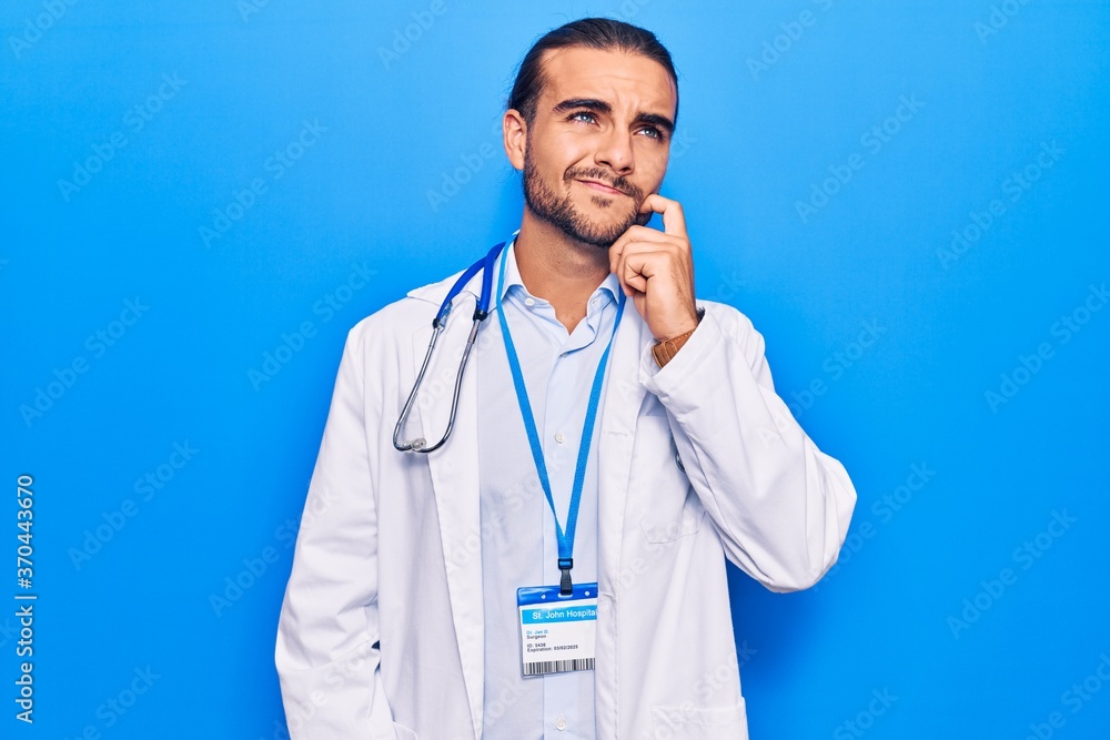 Young handsome man wearing doctor coat and stethoscope thinking concentrated about doubt with finger on chin and looking up wondering Young handsome man wearing doctor coat and stethoscope thinking concentrated about doubt with finger on chin and looking up wondering