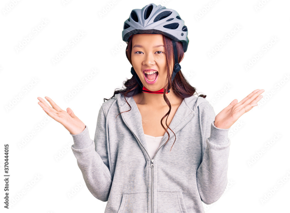 Young beautiful chinese girl wearing bike helmet celebrating victory with happy smile and winner expression with raised hands Young beautiful chinese girl wearing bike helmet celebrating victory with happy smile and winner expression with raised hands