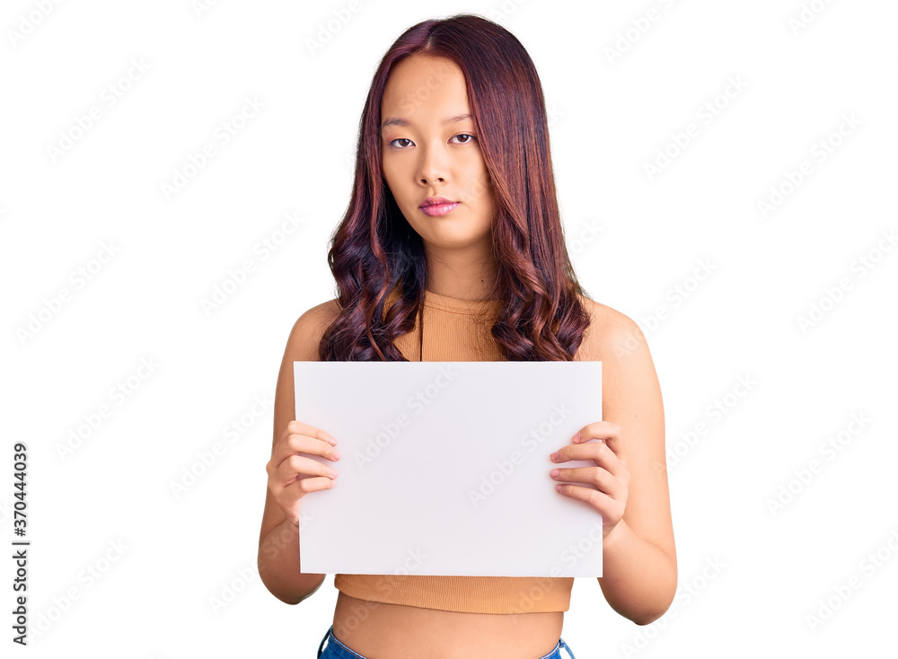 Young beautiful chinese girl holding paper banner with blank space thinking attitude and sober expression looking self confident Young beautiful chinese girl holding paper banner with blank space thinking attitude and sober expression looking self confident