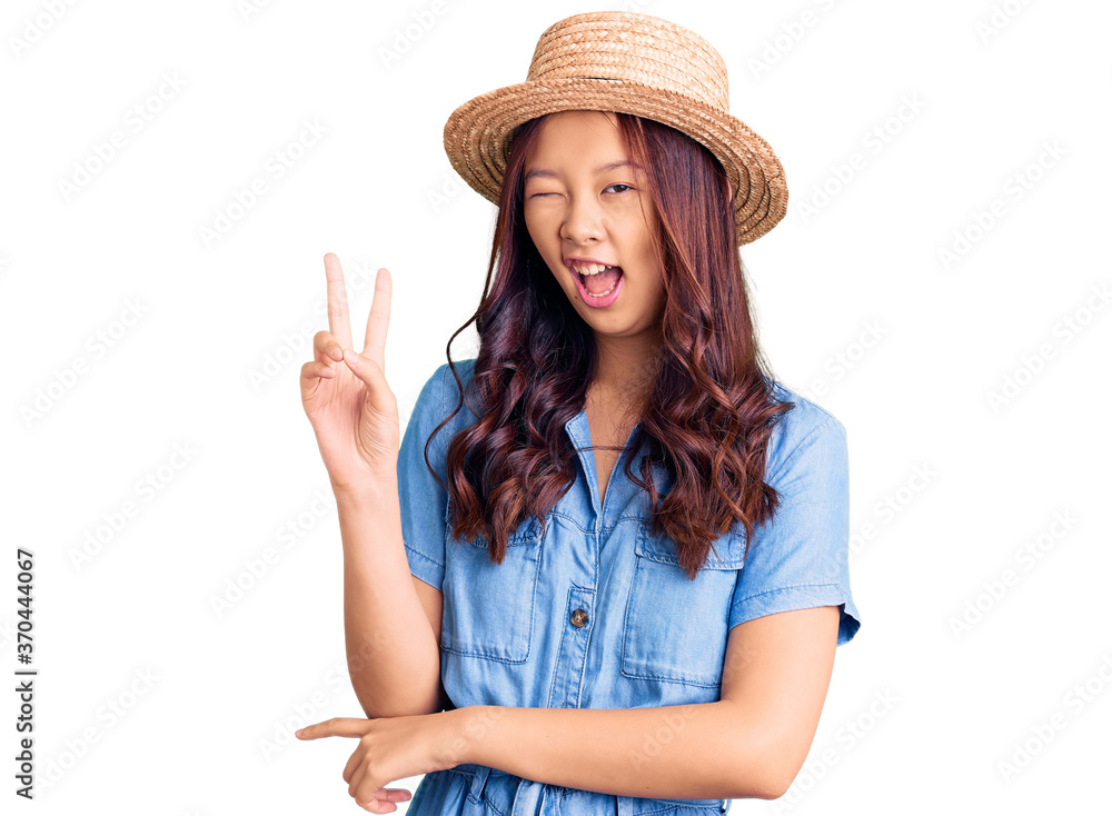 Young beautiful chinese girl wearing summer hat smiling with happy face winking at the camera doing victory sign with fingers. number two. Young beautiful chinese girl wearing summer hat smiling with happy face winking at the camera doing victory sign with fingers. number two.