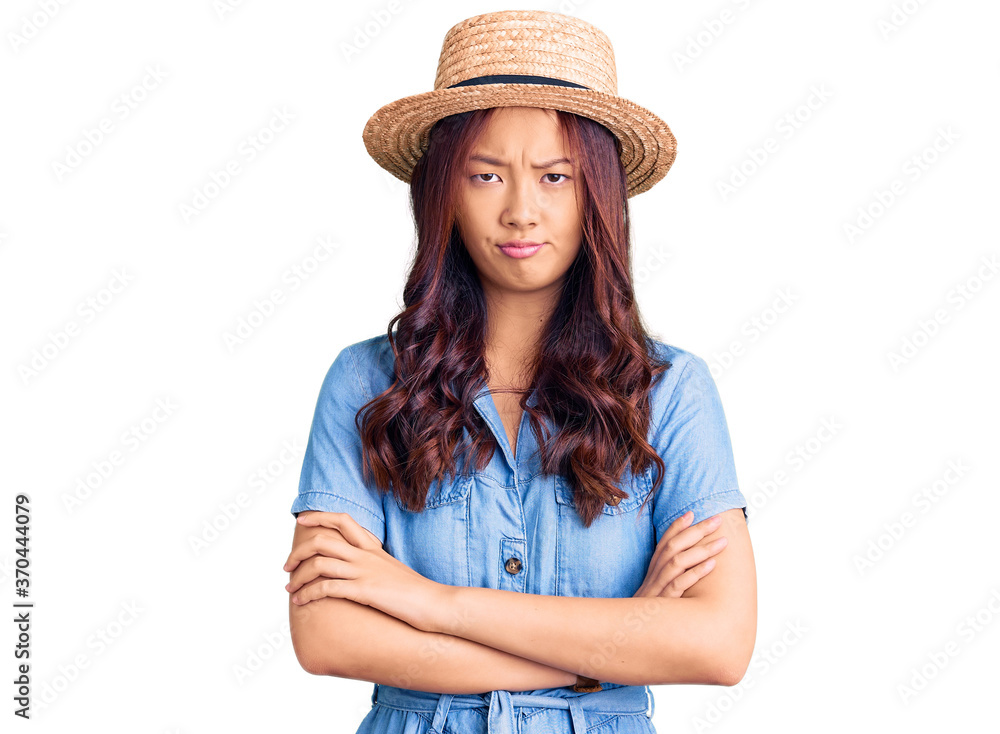 Young beautiful chinese girl wearing summer hat skeptic and nervous, disapproving expression on face with crossed arms. negative person. Young beautiful chinese girl wearing summer hat skeptic and nervous, disapproving expression on face with crossed arms. negative person.