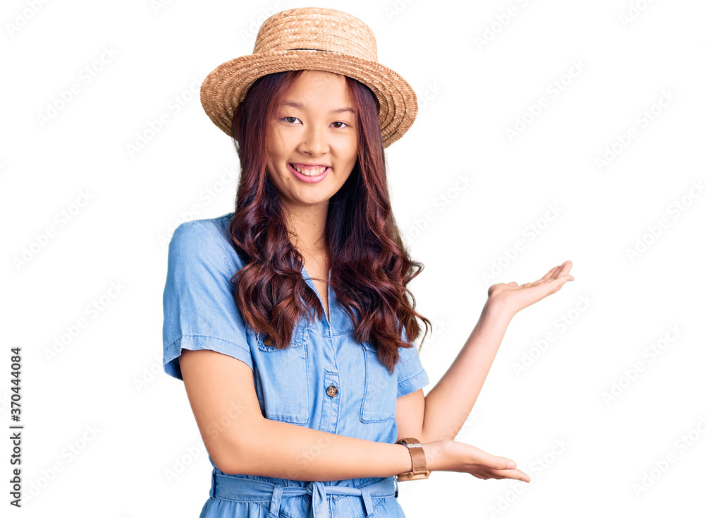 Young beautiful chinese girl wearing summer hat inviting to enter smiling natural with open hand Young beautiful chinese girl wearing summer hat inviting to enter smiling natural with open hand