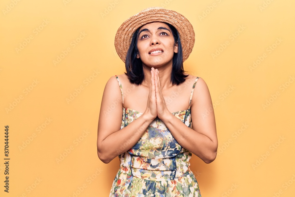 Young beautiful latin woman wearing summer hat begging and praying with hands together with hope expression on face very emotional and worried. begging. Young beautiful latin woman wearing summer hat begging and praying with hands together with hope expression on face very emotional and worried. begging.