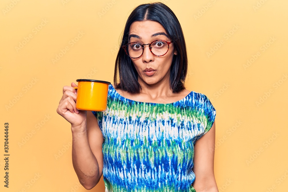Young beautiful latin woman wearing glasses holding coffee scared and amazed with open mouth for surprise, disbelief face Young beautiful latin woman wearing glasses holding coffee scared and amazed with open mouth for surprise, disbelief face