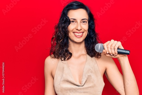 Young beautiful hispanic woman singing song using microphone looking positive and happy standing and smiling with a confident smile showing teeth