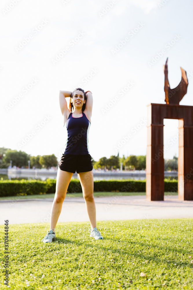 Happy young brunette female exercising and stretching in the park
