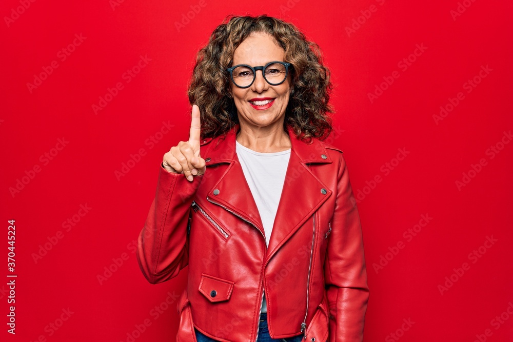 Middle age beautiful woman wearing casual red jacket and glasses over isolated background smiling with an idea or question pointing finger up with happy face, number one