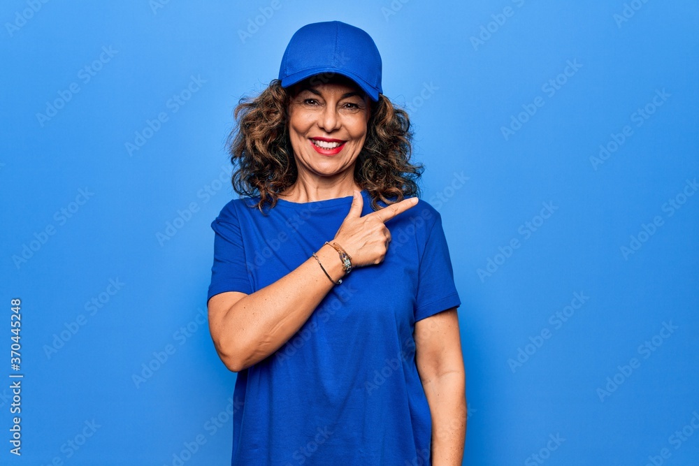 Middle age beautiful delivery woman wearing blue uniform and cap over isolated background smiling cheerful pointing with hand and finger up to the side Middle age beautiful delivery woman wearing blue uniform and cap over isolated background smiling cheerful pointing with hand and finger up to the side