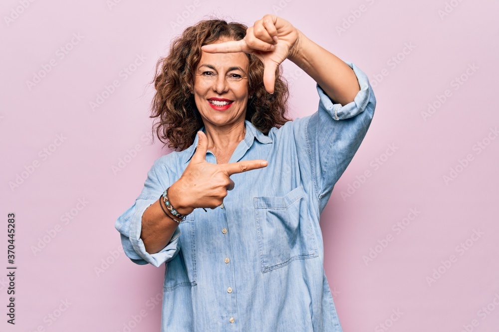 Middle age beautiful woman wearing casual denim shirt standing over pink background smiling making frame with hands and fingers with happy face. Creativity and photography concept. Middle age beautiful woman wearing casual denim shirt standing over pink background smiling making frame with hands and fingers with happy face. Creativity and photography concept.
