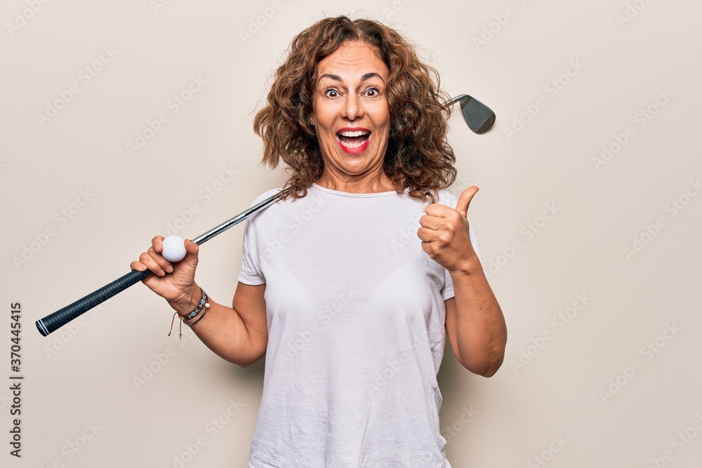 Middle age beautiful sportswoman playing golf using stick and ball over white background pointing thumb up to the side smiling happy with open mouth Middle age beautiful sportswoman playing golf using stick and ball over white background pointing thumb up to the side smiling happy with open mouth