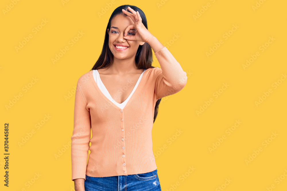 Young beautiful latin girl wearing casual clothes smiling happy doing ok sign with hand on eye looking through fingers Young beautiful latin girl wearing casual clothes smiling happy doing ok sign with hand on eye looking through fingers