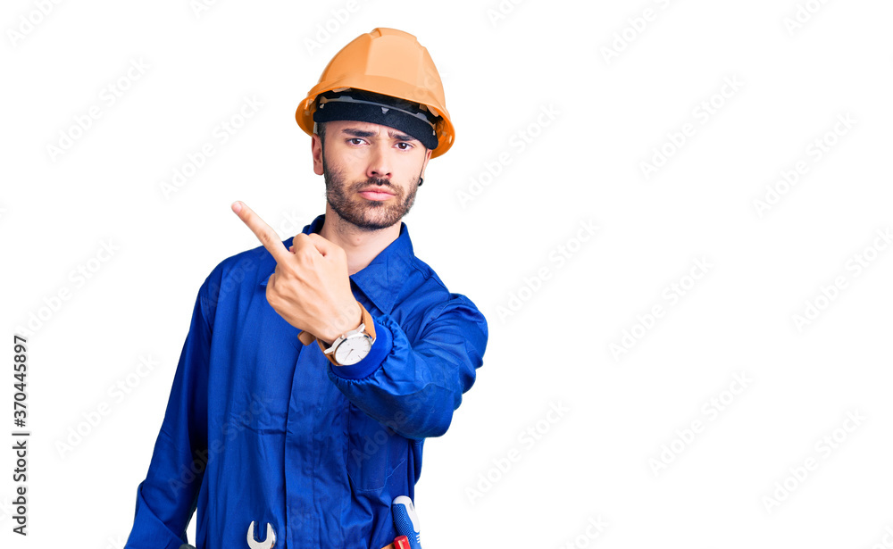 Young hispanic man wearing worker uniform showing middle finger, impolite and rude fuck off expression Young hispanic man wearing worker uniform showing middle finger, impolite and rude fuck off expression