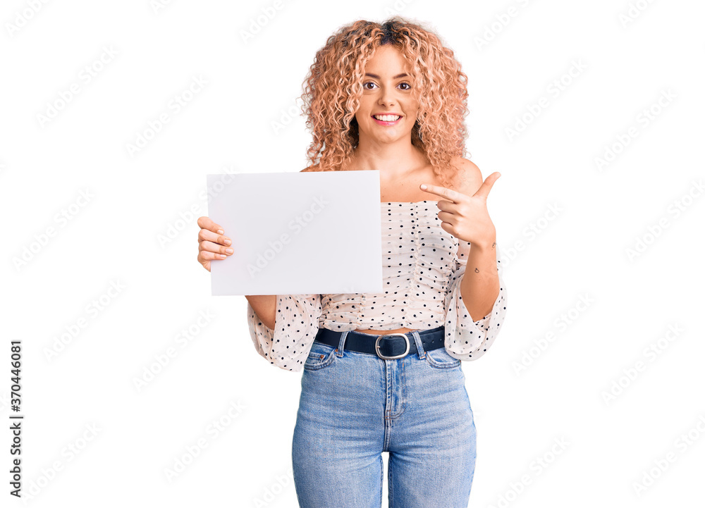 Young blonde woman with curly hair holding sale poster smiling happy pointing with hand and finger Young blonde woman with curly hair holding sale poster smiling happy pointing with hand and finger