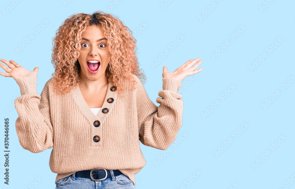Young blonde woman with curly hair wearing casual winter jumper celebrating crazy and amazed for success with arms raised and open eyes screaming excited. winner concept Young blonde woman with curly hair wearing casual winter jumper celebrating crazy and amazed for success with arms raised and open eyes screaming excited. winner concept