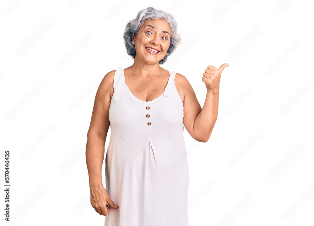 Senior woman with gray hair wearing casual clothes smiling with happy face looking and pointing to the side with thumb up. Senior woman with gray hair wearing casual clothes smiling with happy face looking and pointing to the side with thumb up.