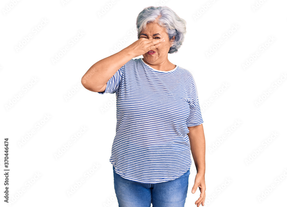 Senior woman with gray hair wearing casual striped clothes smelling something stinky and disgusting, intolerable smell, holding breath with fingers on nose. bad smell Senior woman with gray hair wearing casual striped clothes smelling something stinky and disgusting, intolerable smell, holding breath with fingers on nose. bad smell