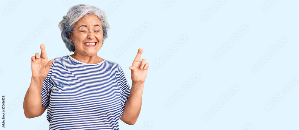 Senior woman with gray hair wearing casual striped clothes gesturing finger crossed smiling with hope and eyes closed. luck and superstitious concept. Senior woman with gray hair wearing casual striped clothes gesturing finger crossed smiling with hope and eyes closed. luck and superstitious concept.