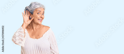 Senior woman with gray hair wearing bohemian style smiling with hand over ear listening an hearing to rumor or gossip. deafness concept. photo