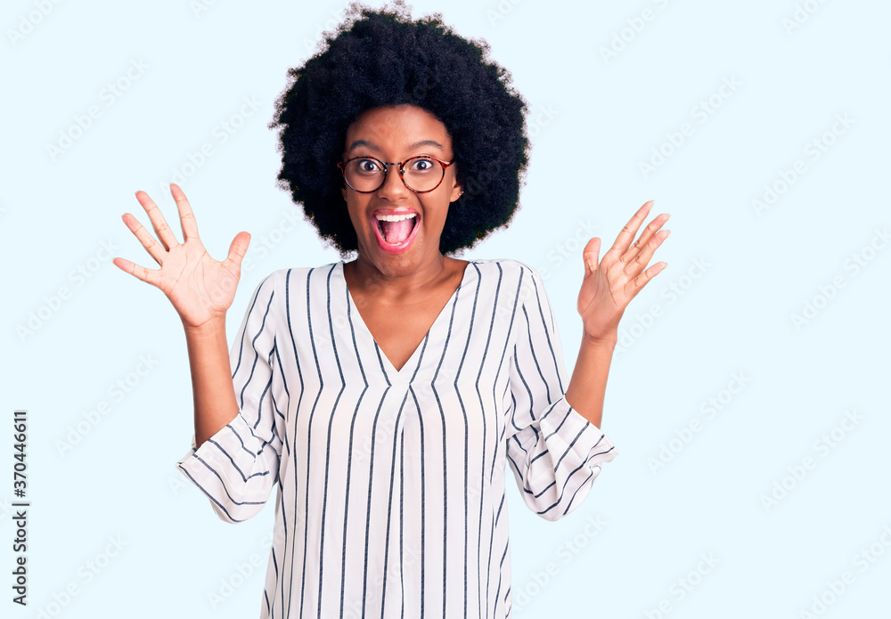 Young african american woman wearing casual clothes and glasses celebrating crazy and amazed for success with arms raised and open eyes screaming excited. winner concept Young african american woman wearing casual clothes and glasses celebrating crazy and amazed for success with arms raised and open eyes screaming excited. winner concept