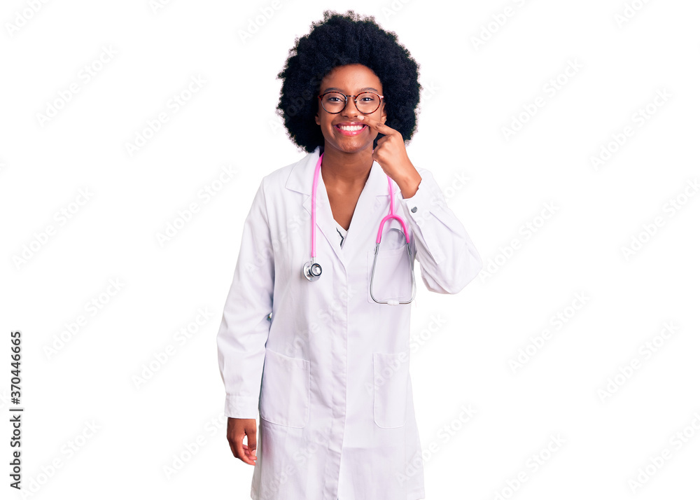 Young african american woman wearing doctor coat and stethoscope pointing with hand finger to face and nose, smiling cheerful. beauty concept Young african american woman wearing doctor coat and stethoscope pointing with hand finger to face and nose, smiling cheerful. beauty concept