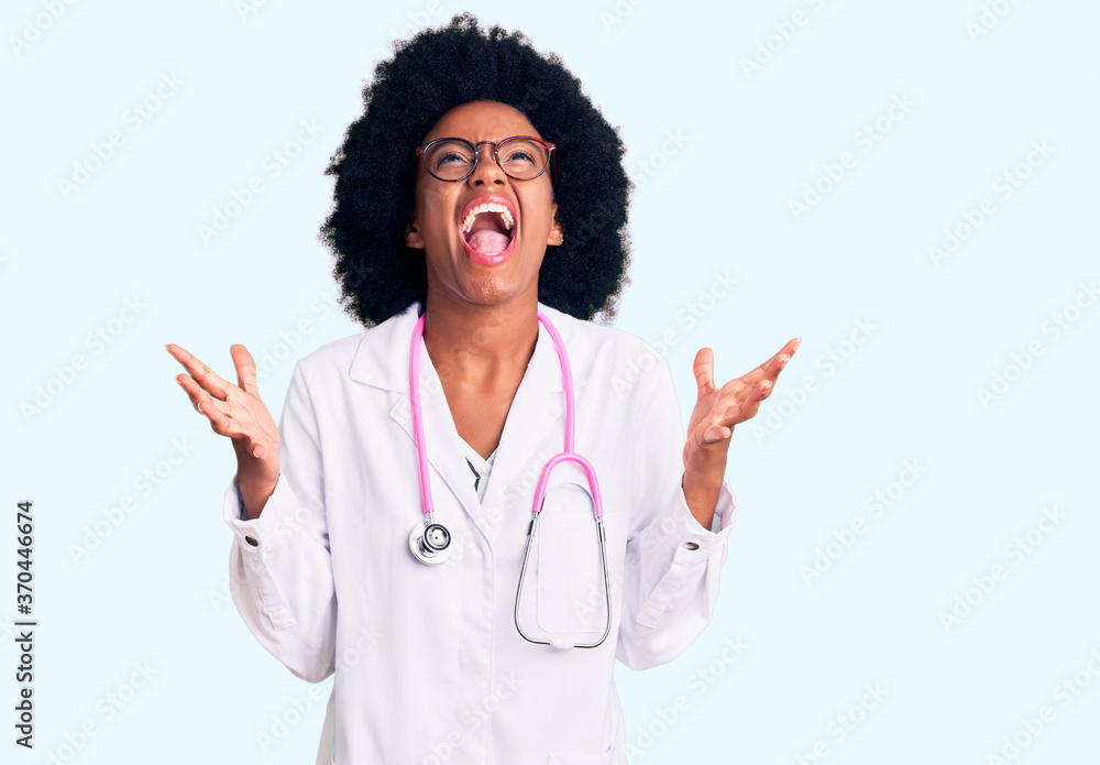 Young african american woman wearing doctor coat and stethoscope celebrating mad and crazy for success with arms raised and closed eyes screaming excited. winner concept Young african american woman wearing doctor coat and stethoscope celebrating mad and crazy for success with arms raised and closed eyes screaming excited. winner concept