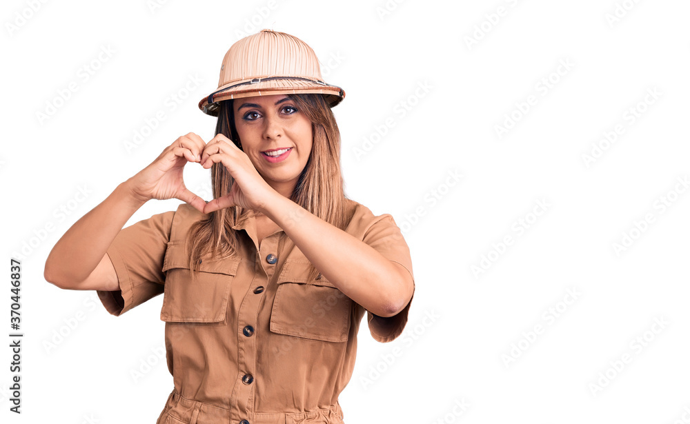 Young beautiful woman wearing explorer hat smiling in love showing heart symbol and shape with hands. romantic concept. Young beautiful woman wearing explorer hat smiling in love showing heart symbol and shape with hands. romantic concept.