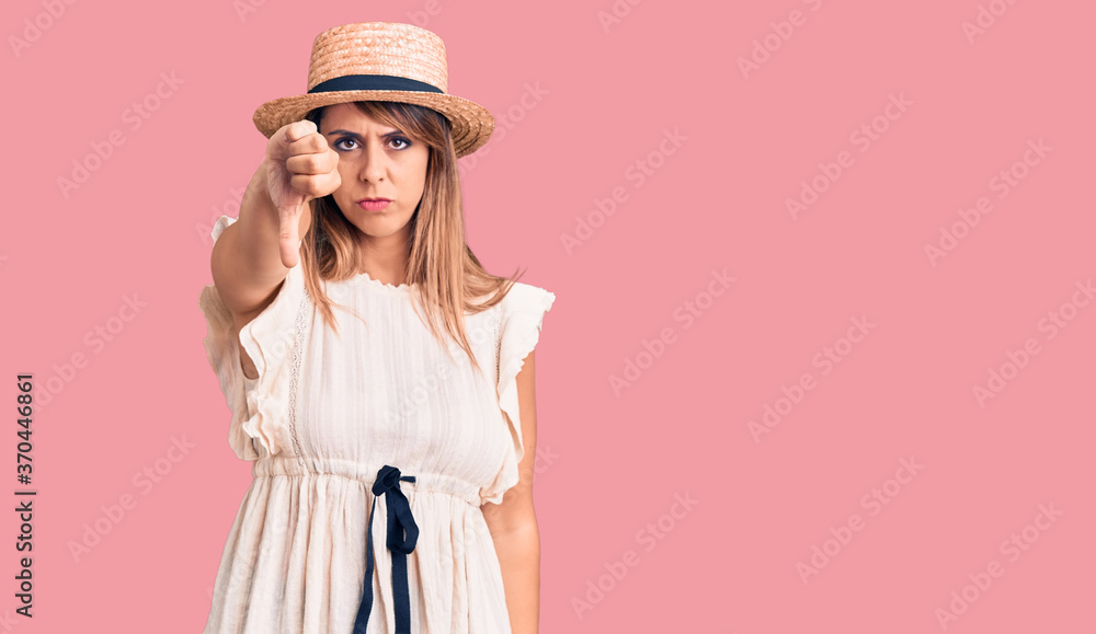 Young beautiful woman wearing summer hat and t-shirt looking unhappy and angry showing rejection and negative with thumbs down gesture. bad expression. Young beautiful woman wearing summer hat and t-shirt looking unhappy and angry showing rejection and negative with thumbs down gesture. bad expression.