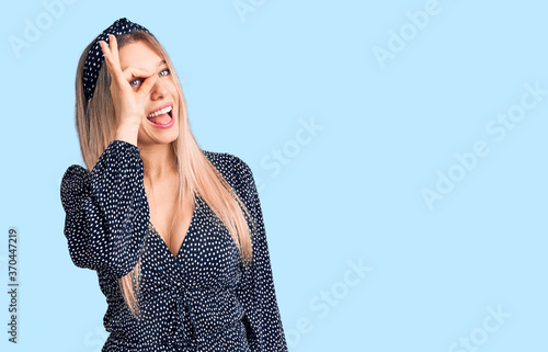 Young beautiful blonde woman wearing casual clothes doing ok gesture with hand smiling, eye looking through fingers with happy face.