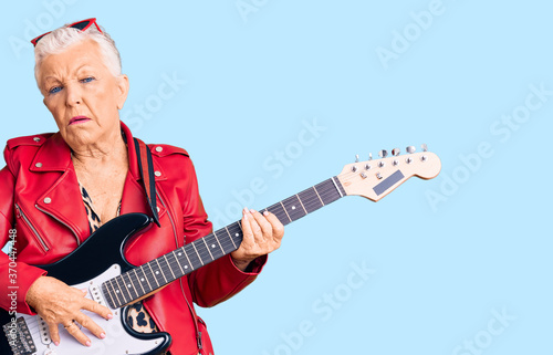 Senior beautiful woman with blue eyes and grey hair wearing a modern look playing electric guitar looking sleepy and tired  exhausted for fatigue and hangover  lazy eyes in the morning.