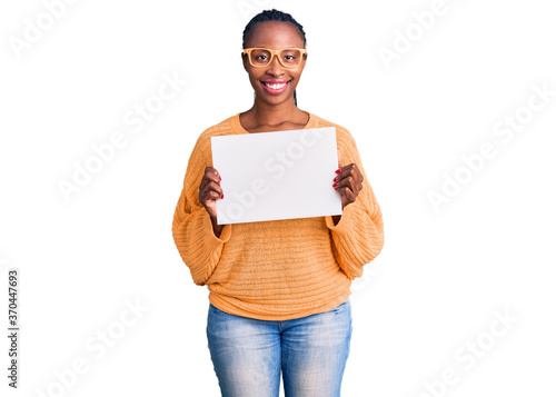 Young african american woman holding cardboard banner with blank space looking positive and happy standing and smiling with a confident smile showing teeth