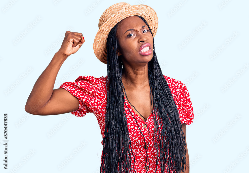 Young african american woman wearing summer hat angry and mad raising fist frustrated and furious while shouting with anger. rage and aggressive concept. Young african american woman wearing summer hat angry and mad raising fist frustrated and furious while shouting with anger. rage and aggressive concept.