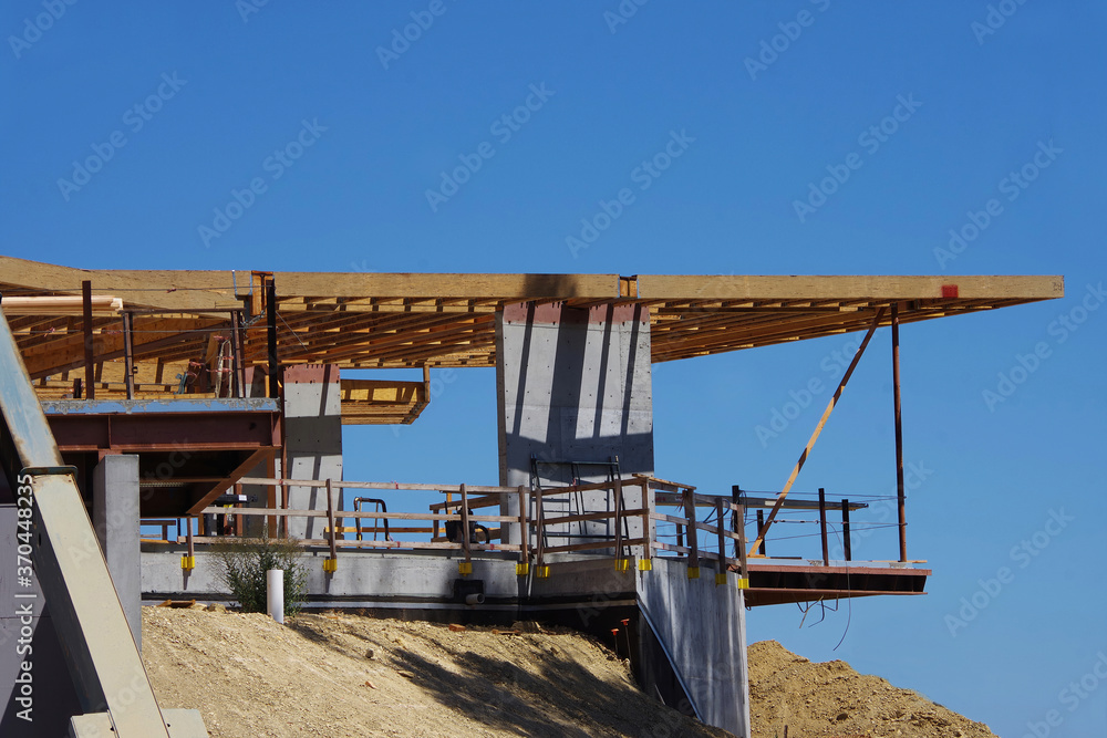 Partial view of a modern cantilever style building under construction on a sunny summer day with blue sky