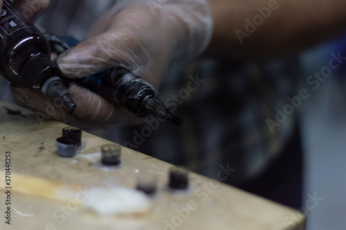 Tattoo artist holding a tattoo machine and dip into inks for tattooing