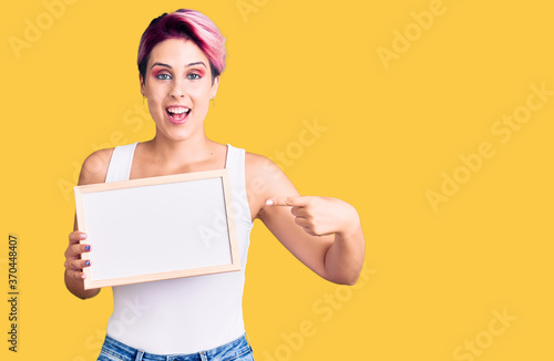 Young beautiful woman with pink hair holding empty white chalkboard smiling happy pointing with hand and finger