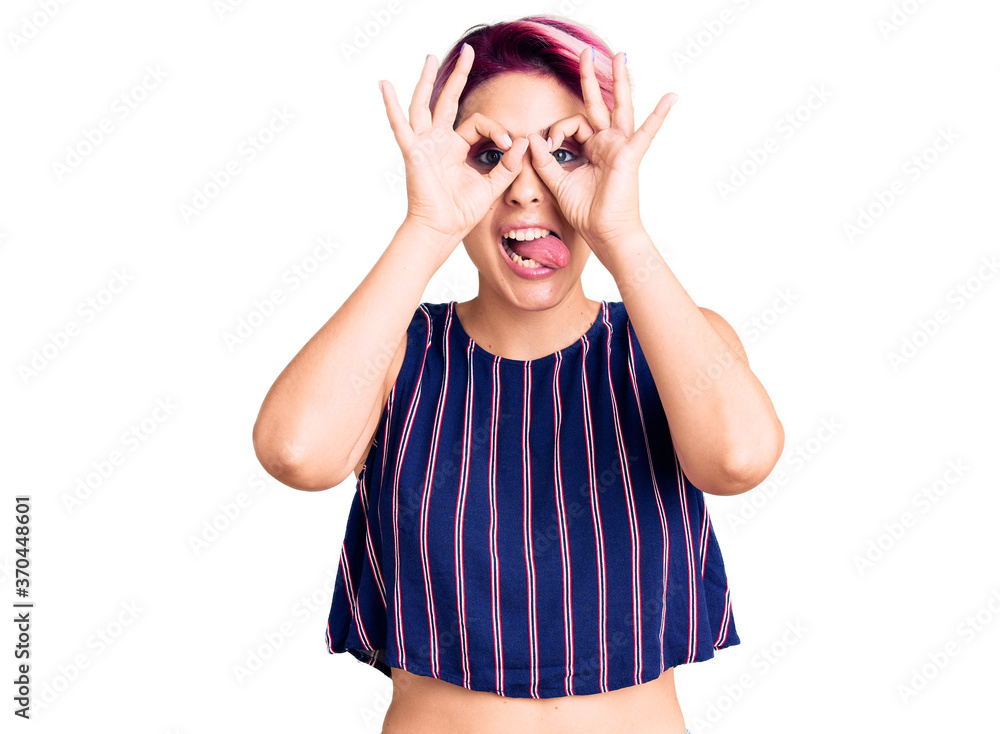 Young beautiful woman with pink hair wearing casual clothes doing ok gesture like binoculars sticking tongue out, eyes looking through fingers. crazy expression. Young beautiful woman with pink hair wearing casual clothes doing ok gesture like binoculars sticking tongue out, eyes looking through fingers. crazy expression.