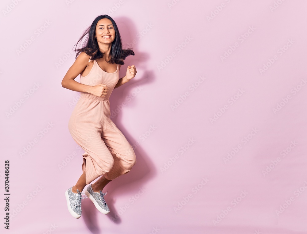 Young beautiful latin woman wearing casual clothes smiling happy. Jumping with smile on face over isolated pink background