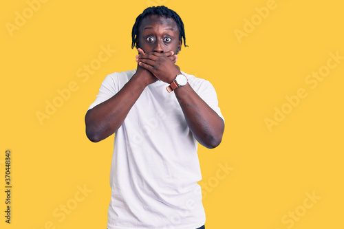 Young african american man with braids wearing casual white tshirt shocked covering mouth with hands for mistake. secret concept.