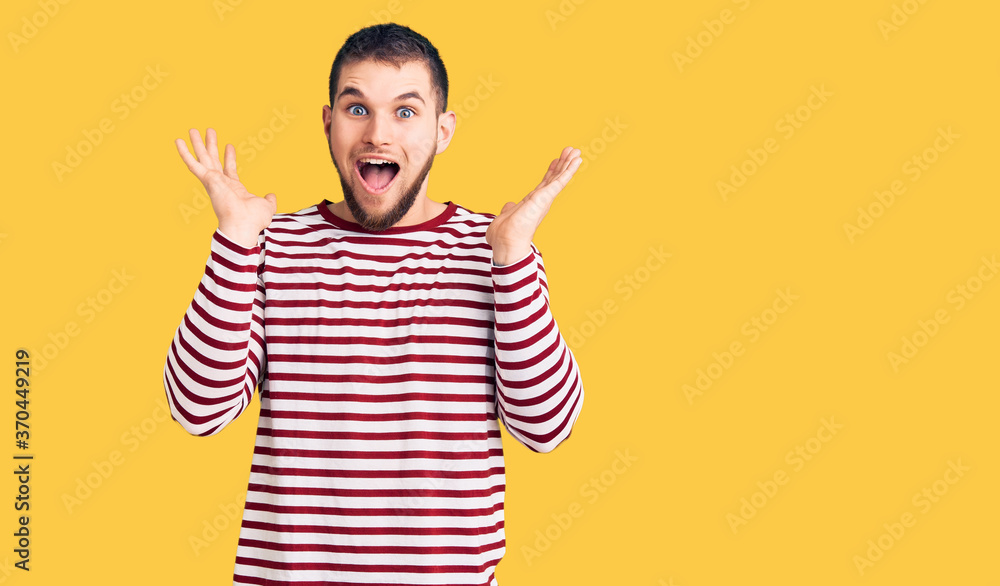 Young handsome man wearing striped sweater celebrating crazy and amazed for success with arms raised and open eyes screaming excited. winner concept Young handsome man wearing striped sweater celebrating crazy and amazed for success with arms raised and open eyes screaming excited. winner concept