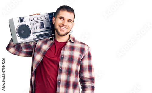 Young handsome man listening to music holding boombox looking positive and happy standing and smiling with a confident smile showing teeth