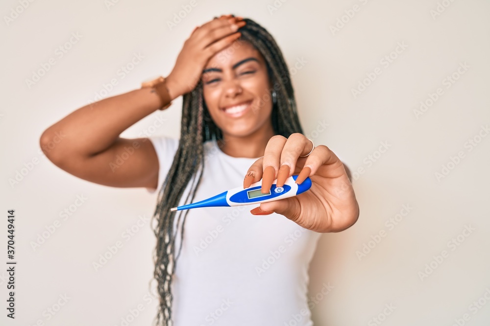 Young african american woman with braids holding thermometer stressed and frustrated with hand on head, surprised and angry face Young african american woman with braids holding thermometer stressed and frustrated with hand on head, surprised and angry face