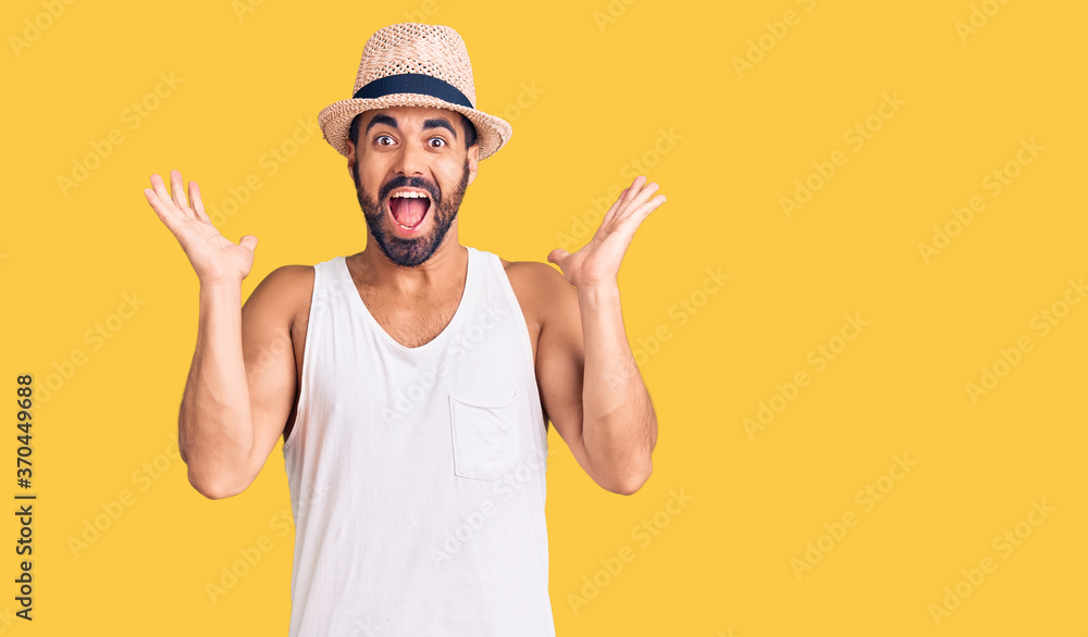 Naklejka premium Young hispanic man wearing casual summer hat celebrating crazy and amazed for success with arms raised and open eyes screaming excited. winner concept