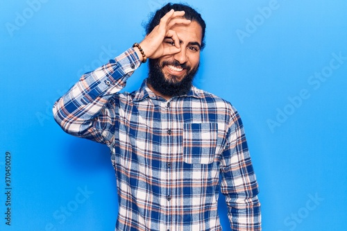 Young arab man wearing casual clothes smiling happy doing ok sign with hand on eye looking through fingers
