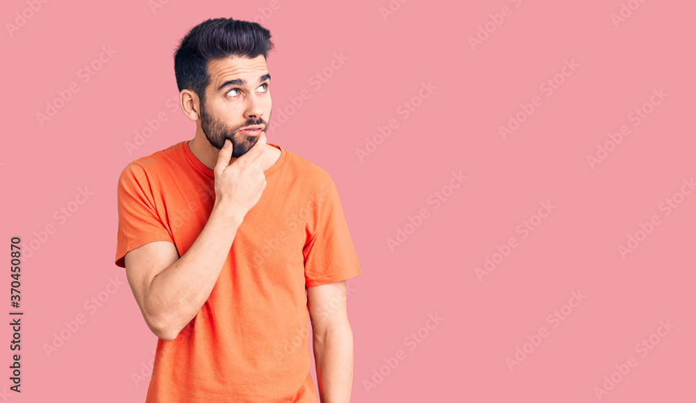 Young handsome man with beard wearing casual t-shirt thinking worried about a question, concerned and nervous with hand on chin Young handsome man with beard wearing casual t-shirt thinking worried about a question, concerned and nervous with hand on chin