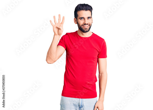 Young handsome man with beard wearing casual t-shirt showing and pointing up with fingers number four while smiling confident and happy.