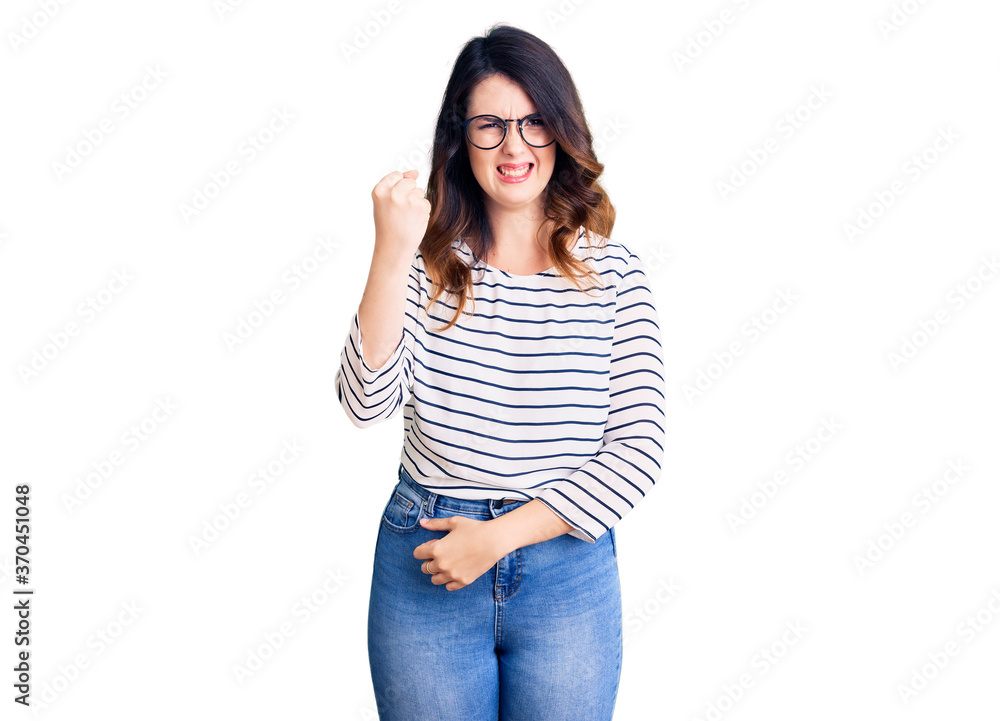 Beautiful young brunette woman wearing casual clothes and glasses angry and mad raising fist frustrated and furious while shouting with anger. rage and aggressive concept. Beautiful young brunette woman wearing casual clothes and glasses angry and mad raising fist frustrated and furious while shouting with anger. rage and aggressive concept.