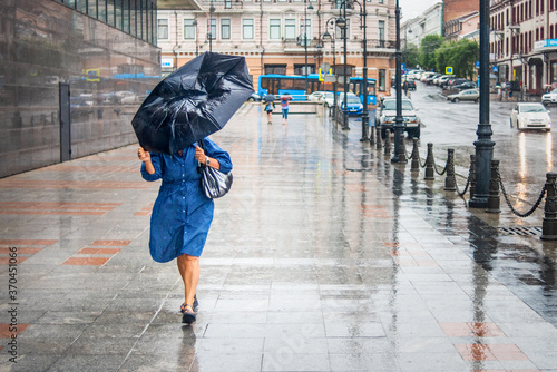 Canvas-taulu Woman in bad rainy weather walks down the street and tries to keep the umbrella from the strong wind